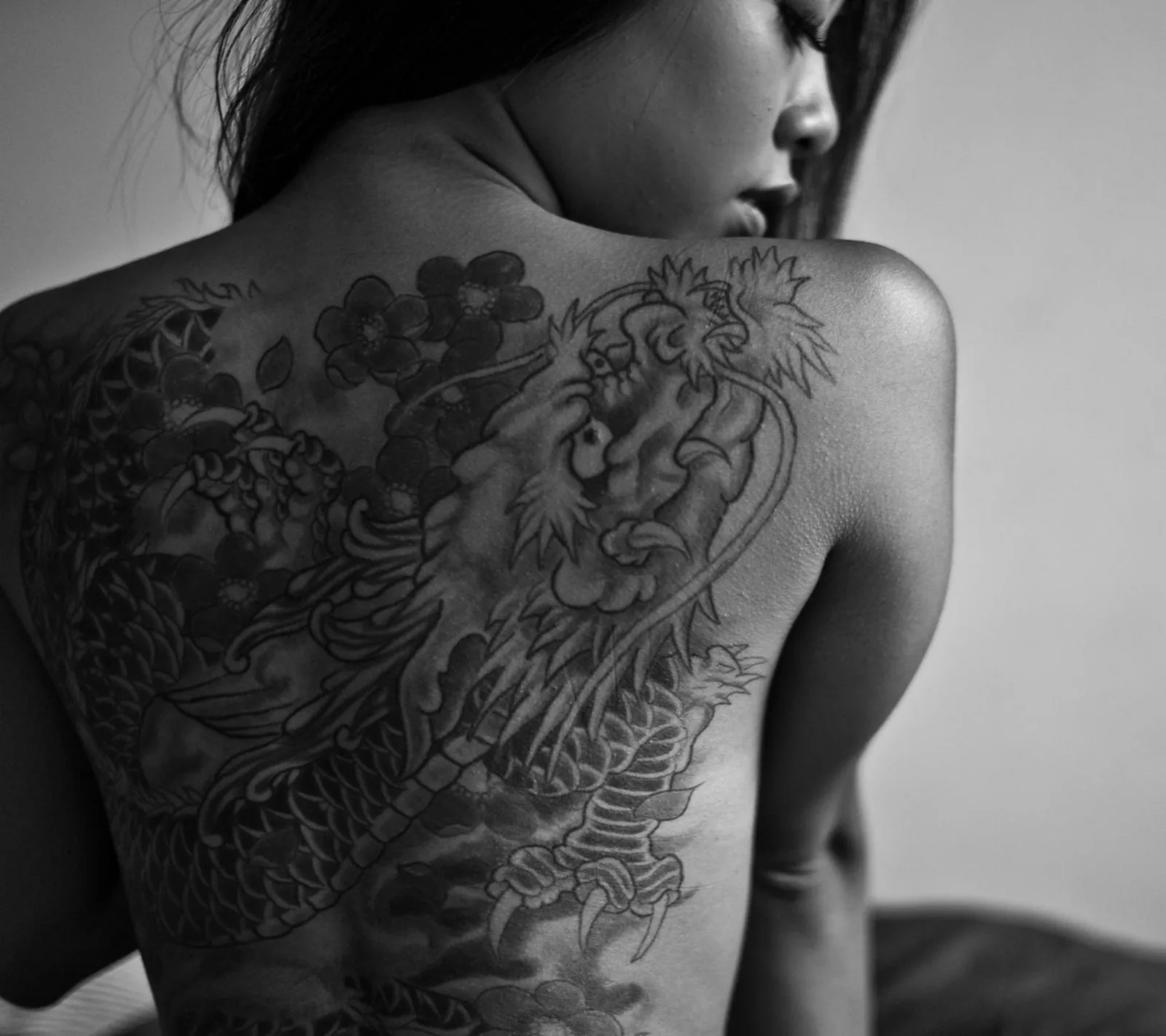 Black and grey dragon and peony back piece on a woman looking over her shoulder