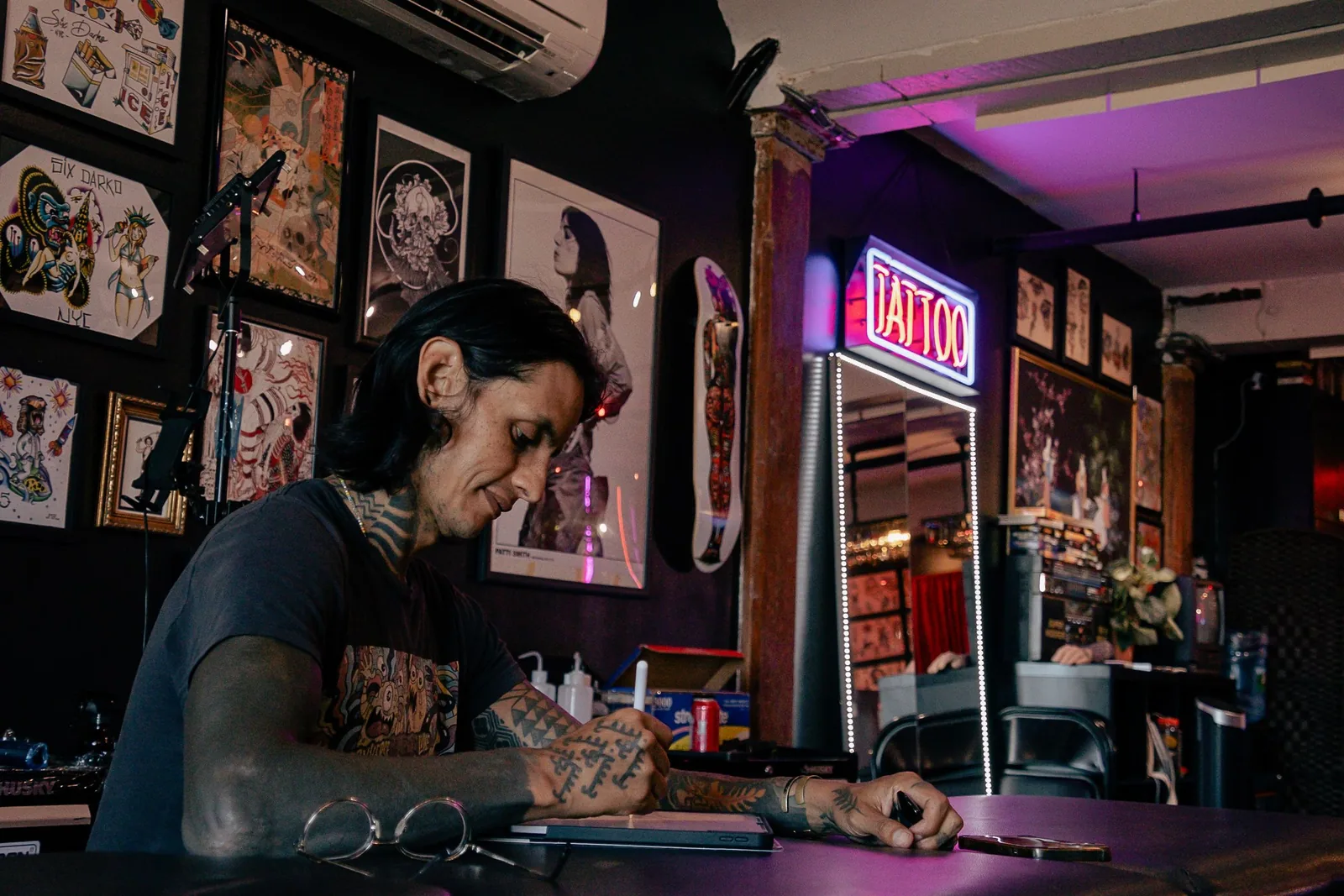 An artist sketching at a desk under a neon sign