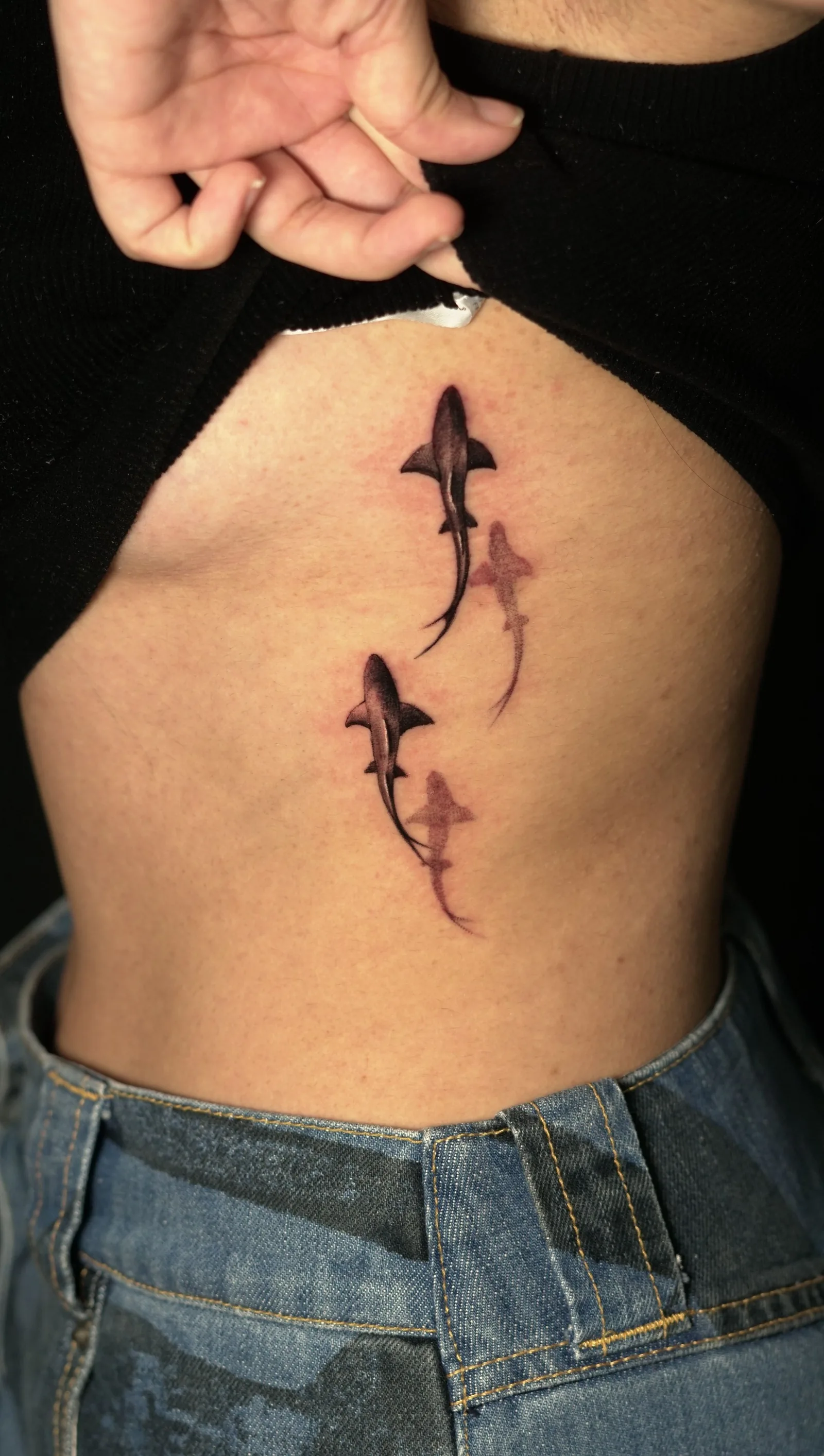 Two small sharks tattooed on a ribcage